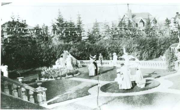 Black and white image of men and women enjoying a garden party, circa 1900.