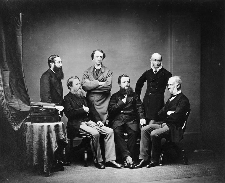 Black and white studio group portrait of six men; three standing and three sitting. The middle standing man is Sir John A. Macdonald.