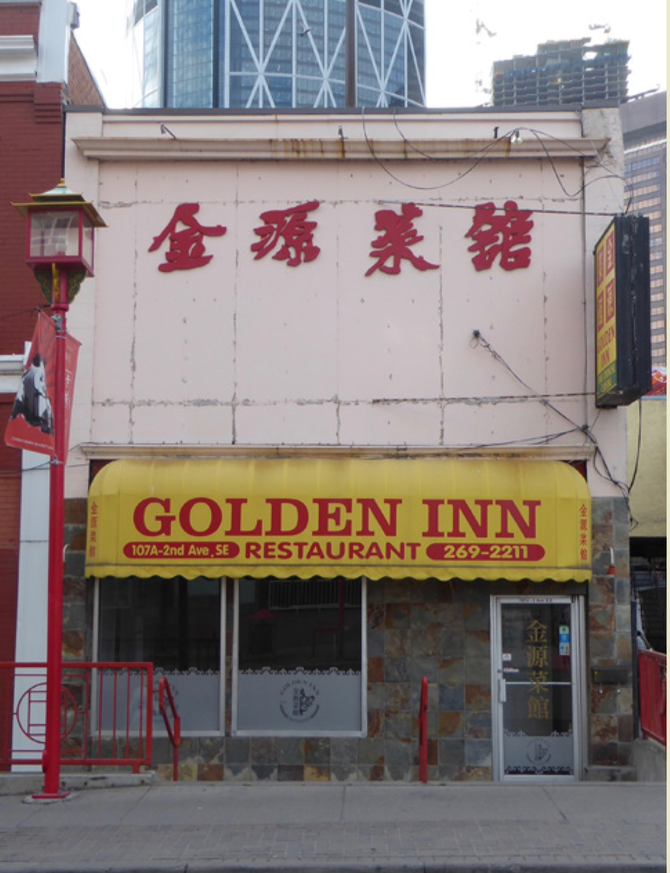 Building front. First floor is a Chinese restaurant with a yellow awning that says "Golden Inn Restaurant". Front façade of top half of building has four red Chinese characters.