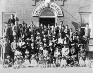 Big group photo of about 50 people in front of building that says "Chinese Mission" above their heads. Black and white.