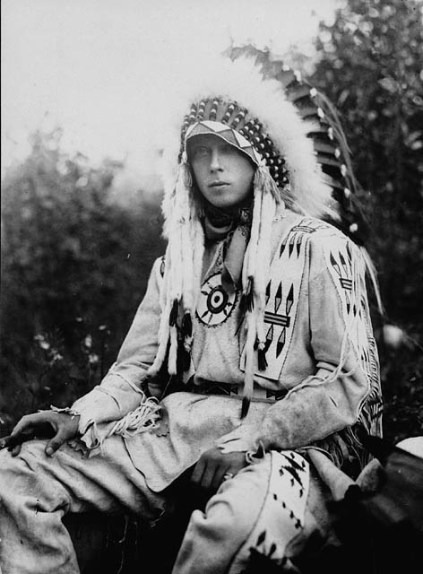 A young Prince of Wales seated wearing a First Nations headdress. Black and white.